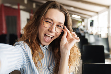 Image of funny beautiful woman winking and taking selfie