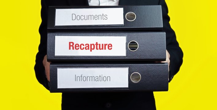 Recapture – finance/economics. Man carries a stack of 3 file folders. A folder has the label Recapture. Business, statistics concept