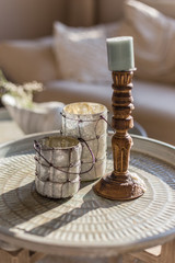 Cozy home concept. Wooden and glass candleholders on a round coffee table.