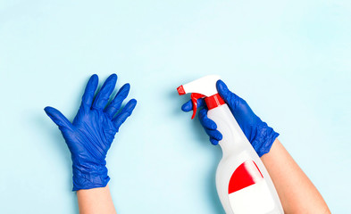 Hands in rubber medical gloves holds a bottle with antiseptic spray on a blue background.