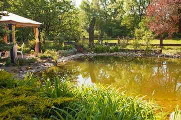 Beautiful pond with goldfishs in a sunny garden with patio, chairs and bench