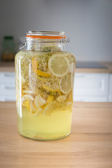 Preparing homemade elderflower syrup. Elder flowers with lemon slices in a glass jar to make a refreshing drink. Vertical shot.