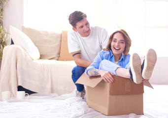 Happy couple having fun and riding in cardboard boxes at new home