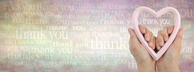 Heart felt thank you background banner -  female hands holding a pink flesh coloured heart frame against a grunge rustic graduated background of many different sized words of thank you 
