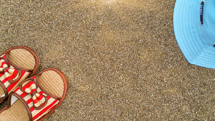 Part of the straw beach sandals and part of the hat on the sand by the sea. Summer holidays. The beach background. Tourist holidays. Concept for the summer season. Flatlay photo. Copy space.
