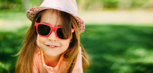 Portrait of a little cute girl wearing a hat and sunglasses outdoors. Copy space.