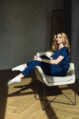 A young blonde is sitting in an arm-chair with her legs up in the sun