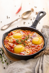 Shakshuka. Fried eggs with tomatoes and sweet pepper and herbs in a serving cast-iron frying pan.