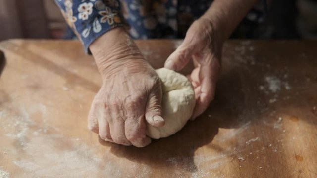 Cooking homemade pastries: grandmother kneads dough on a wooden table