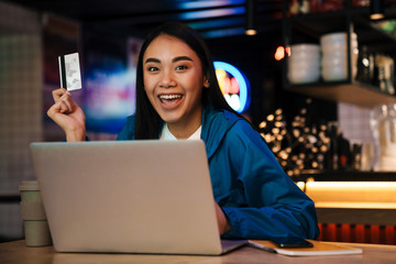 Photo of young asian woman working with laptop and holding credit card