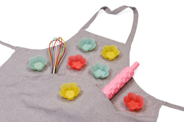 Apron with plastic rolling pin, whisk and silicon muffin cups isolated on white background. View from above