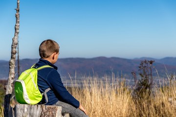 krajobraz górski, chłopak siedzący na pniu patrzący w dal, gdzieś na szlaku