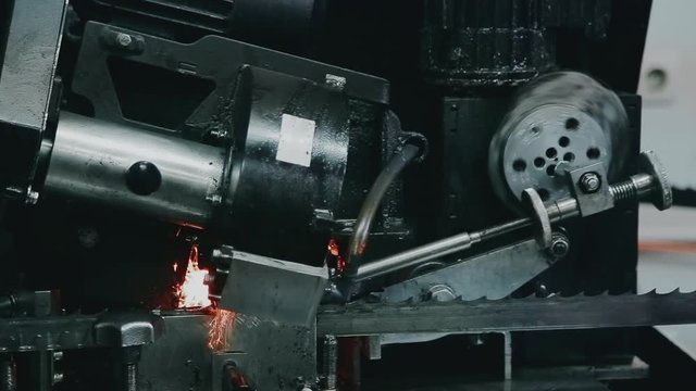 Sharpening of a band saw on an automated grinder, close-up shooting. The grinding disc touches the saw and is dampened with oil, sparks fly.