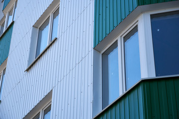 Fototapeta na wymiar facade of a new multi-storey building with white and green metal siding, many Windows