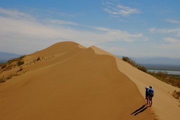 Fototapeta na wymiar Couple walking in top of Singing sand dune inside Ile Altyn Emel National Park
