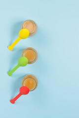 Overhead shot of glass jars of baby food with colorful spoons on blue background