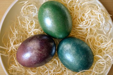 Colourful shiny easter eggs in the bowl with hay. Basket with three painted Easter eggs. Top view, Selective focus
