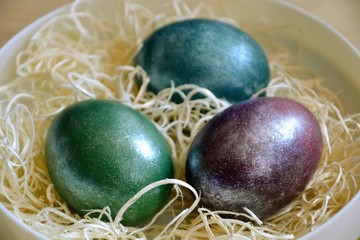 Colourful shiny easter eggs in the bowl with hay. Basket with three painted Easter eggs.Selective focus