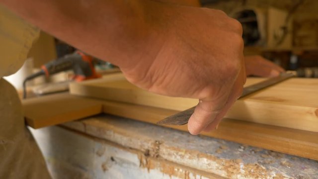 Carpintero sostiene una tabla de madera sobre la mesa de trabajo mientras dibuja una l&iacute;nea con un l&aacute;piz en la tabla con la ayuda de una escuadra en su taller de carpinter&iacute;a.