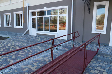 Wheelchair access ramp for entrance of residential multistory building, city street and tiles sidewalk