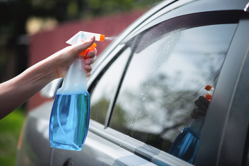 Cleaner is cleaning a car window glass with a rag and detergent close up.