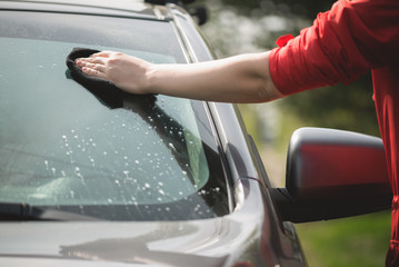 Cleaner is cleaning a car window glass with a rag and detergent close up.