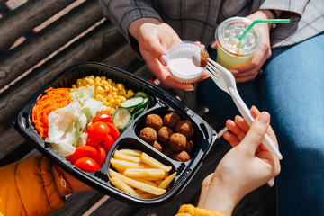Close up of hands of two young adult woman sharing and eating food on the go - together in a public park.