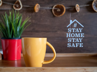 STAY HOME STAY SAFE message on wooden texture with yellow cup and red flower pot