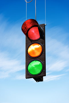 Traffic Light On A Blue Sky With Clouds, With All Three Lights On, Green, Orange And Red.