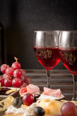 glasses of red wine , slices of cheese, cracker, ham, jam, grapes, olives,  on a dark wooden background, appetizer, tapas, copy space,