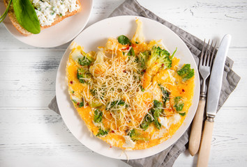 omelet with cheese, spinach,  broccoli,  on a white plate, sandwich with cheese and greens on a white wooden background, knife, fork, napkin, close up