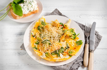 omelet with cheese, broccoli, spinach on a white plate, sandwich with cheese and greens on a white wooden , knife, fork, napkin