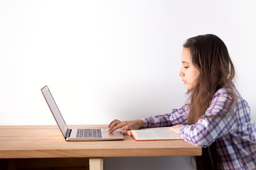 Distance learning at home. Teen girl with laptop does homework, reads a book, search information on the Internet. Elearning concept.