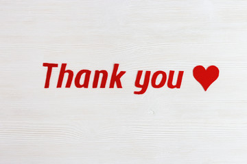 Text "thank you" and red colored heart on white wooden background with copy space. Words of gratitude and expressions of love. View from above.