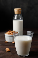 Almond milk in a glass and a glass bottle on dark wooden background