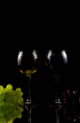 Grapes are on the table. Next to it are two glasses in which red and white wine is poured
