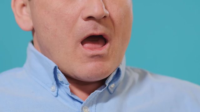 man with glasses in shirt sneezes into arm bend standing against blue background slow motion closeup