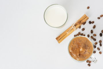 Dalgona Coffee Iced, a Korean fashionable whipped black instant coffee with milk, on a white background with coffee beans, cinnamon sticks, chocolate chips. Copy space. Top view.