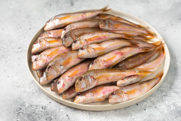 Black sea barabulka fish in a white ceramic bowl on a light gray kitchen table. A lot of fish red mullet. Black sea barabulka