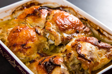 Baked chicken thighs with onions in ceramic form on a stone table, copy space.