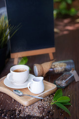 a white cub of coffee with a white cub of honey on wooden plate, background with wooden black board