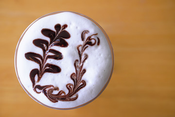 a close up top view of topping cream pattern on a cub of coffee on wooden floor