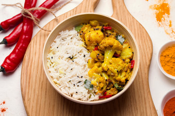 Gobi Aloo traditional Indian dish of cauliflower and potato with rice on a wooden board