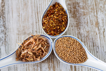 Spices and herbs in porcelain spoons over a wooden background