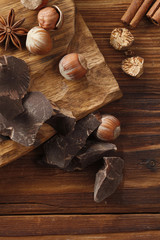 Background of chocolate pieces , cinnamon, stars anise and hazelnuts on a wooden table. Chipped Dark Chocolate Pattern. Top view