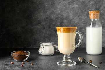 Iced Dalgona coffee in glass mug on dark table. Trendy refreshment creamy whipped Macau coffee. Korean coffee drink. Horizontal orientation, copy space