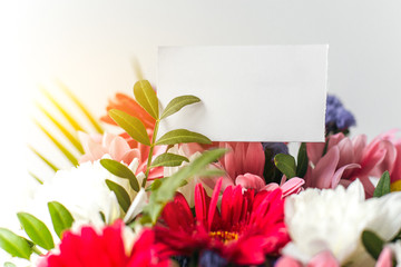 beautiful bright colorful flower bouquet with paper blank white gift card, place for text, sun ray 