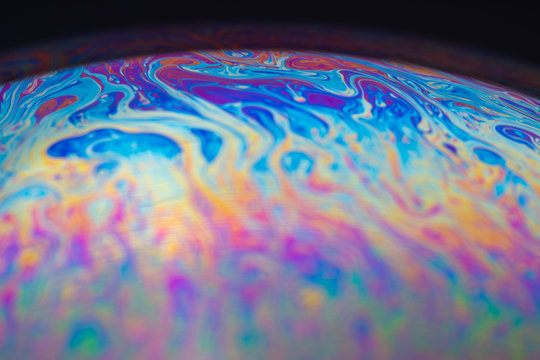 Soap bubble iridescent colors close-up on the surface of the iridescent spots. Round sphere planet-like abstraction.