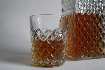 drink strong alcoholic cognac or whiskey in a glass crystal glass next to a decanter on a white...