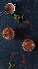 Tiramisu in a transparent with cocoa and mint on a blue dark background. Top view, flat lay.